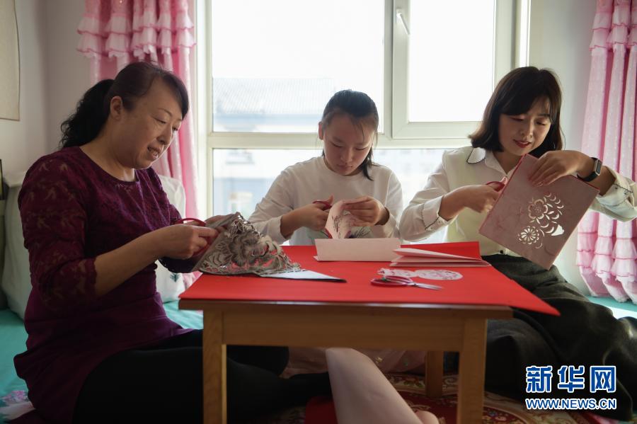 　　2月21日，在烏海市海南區(qū)新橋花園，李華（左）與外孫女高宇晨（中）、大女兒譚紅葉一起在家中剪紙。新華社記者 李志鵬 攝
